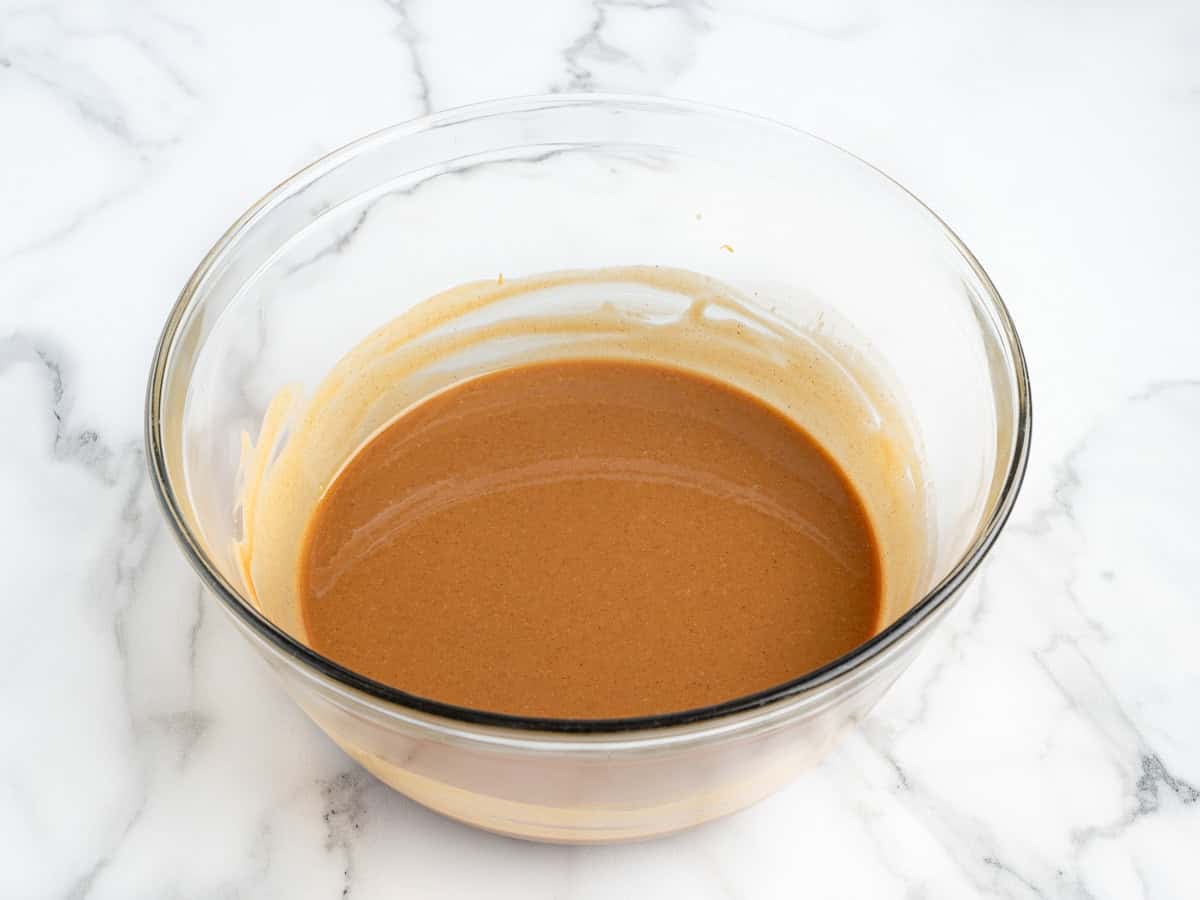 A glass bowl filled with smooth, light brown batter for Peanut Butter Fudge (Microwave) sits on a white marble surface.
