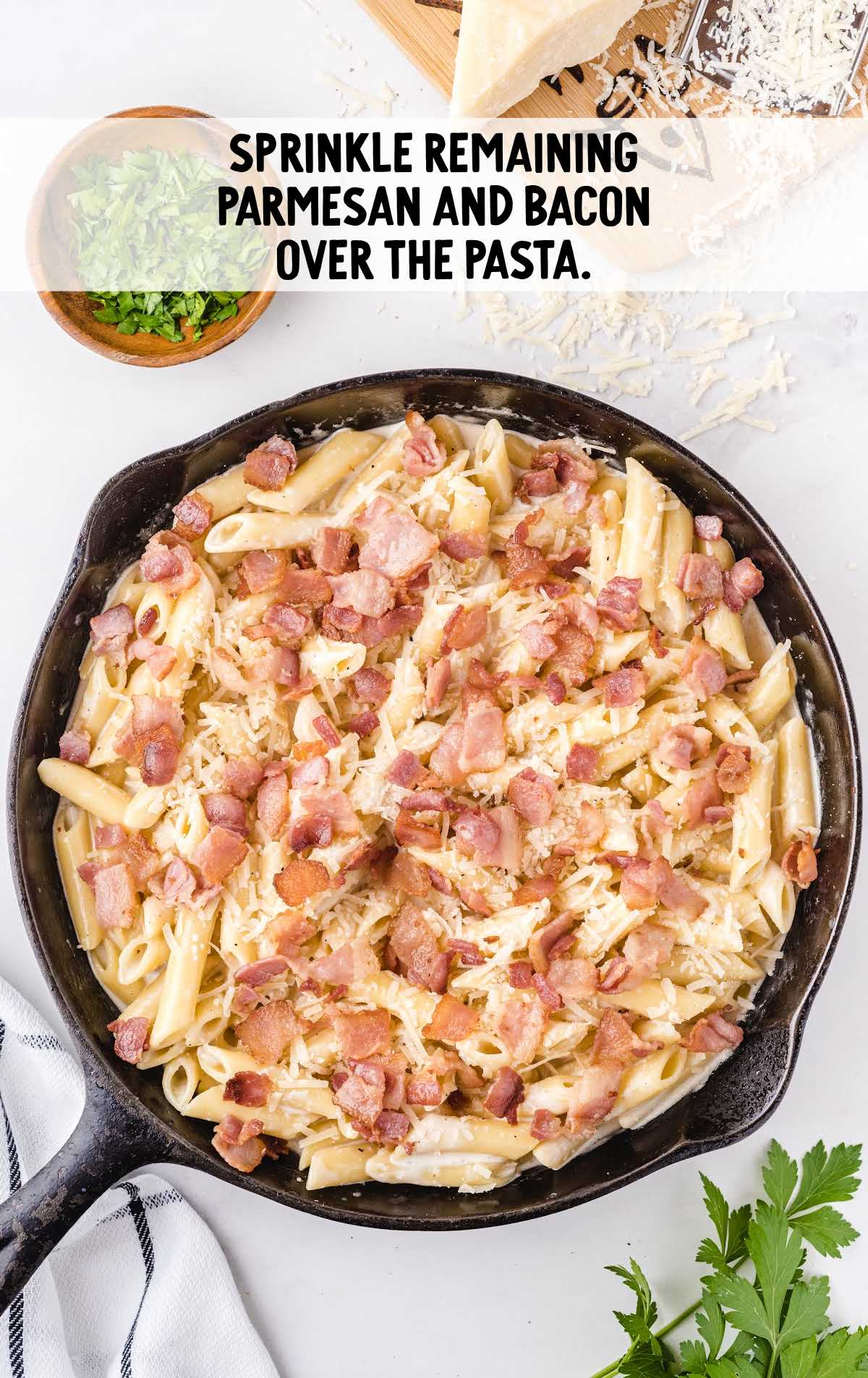 parmesan cheese and bacon sprinkled over the pasta in a skillet