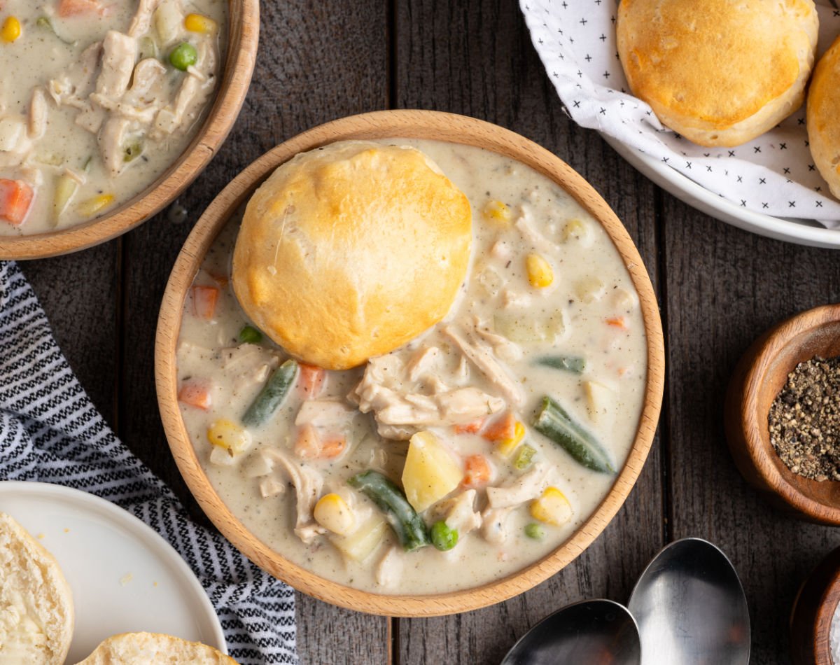 Bowl of chicken pot pie soup topped with a biscuit, showing chunks of chicken, potatoes, and vegetables in a creamy broth.