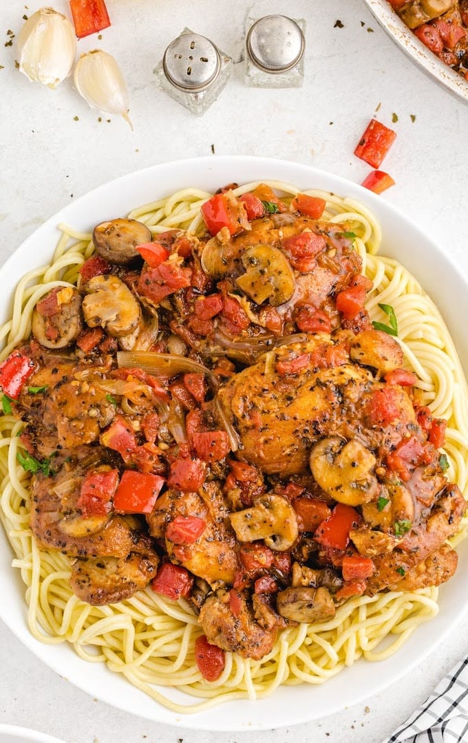 overhead shot of chicken cacciatore on a white plate served over pasta