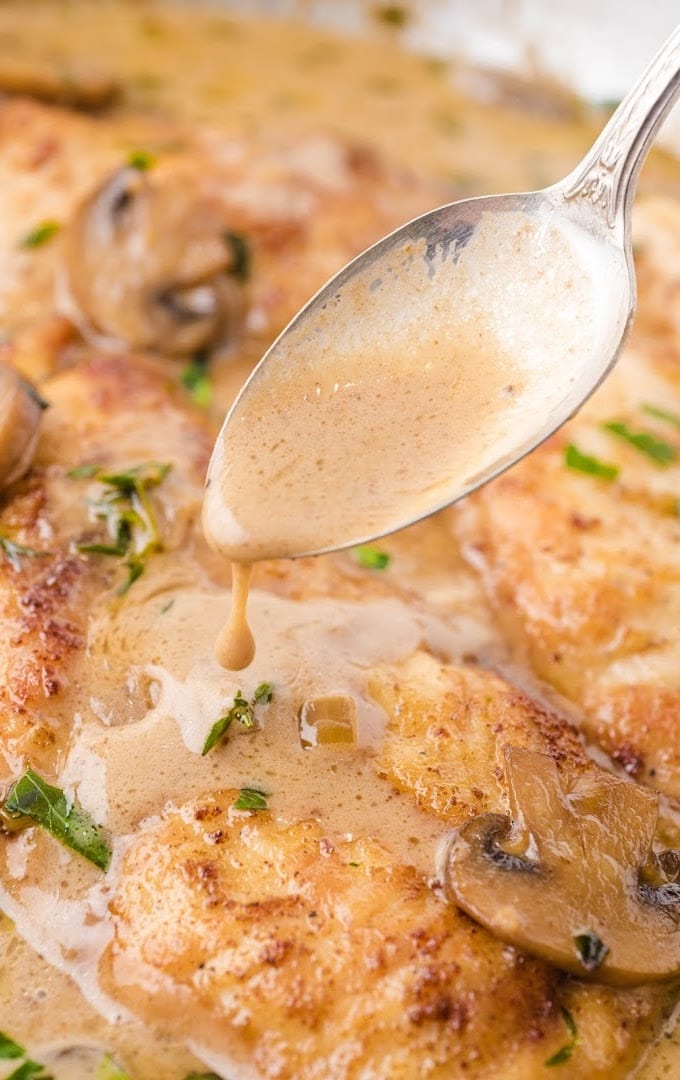 close up shot of a spoon pouring glaze on chicken marsala
