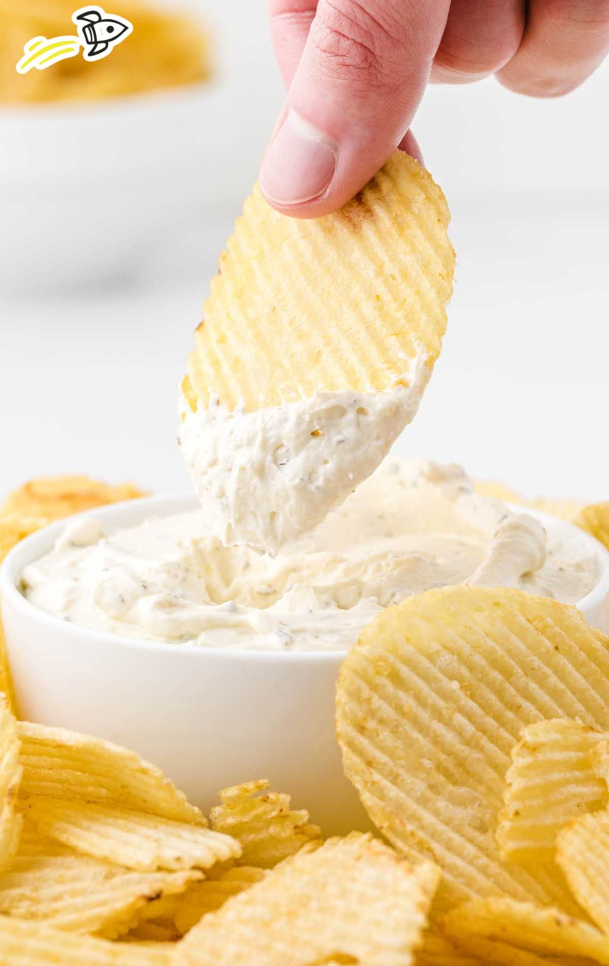 close up shot of chip dip in a dish surrounded by chips and being dipped