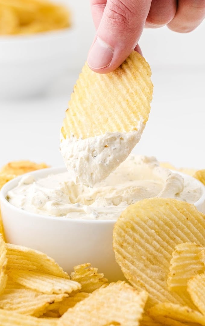 close up shot of chip dip in a dish surrounded by chips and being dipped