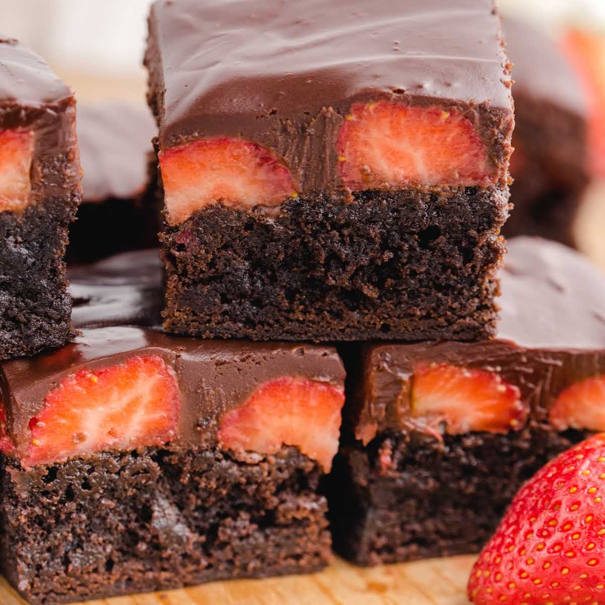 close up shot of Chocolate Covered Strawberry Brownies stacked on top of each other on a wooden board
