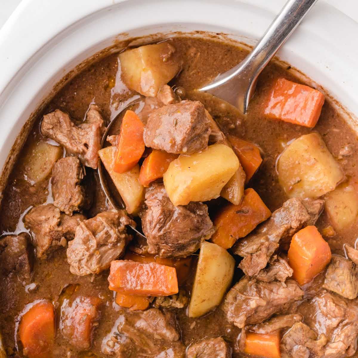 Overhead view of crockpot beef stew showing beef, carrots, and potatoes in a rich sauce.