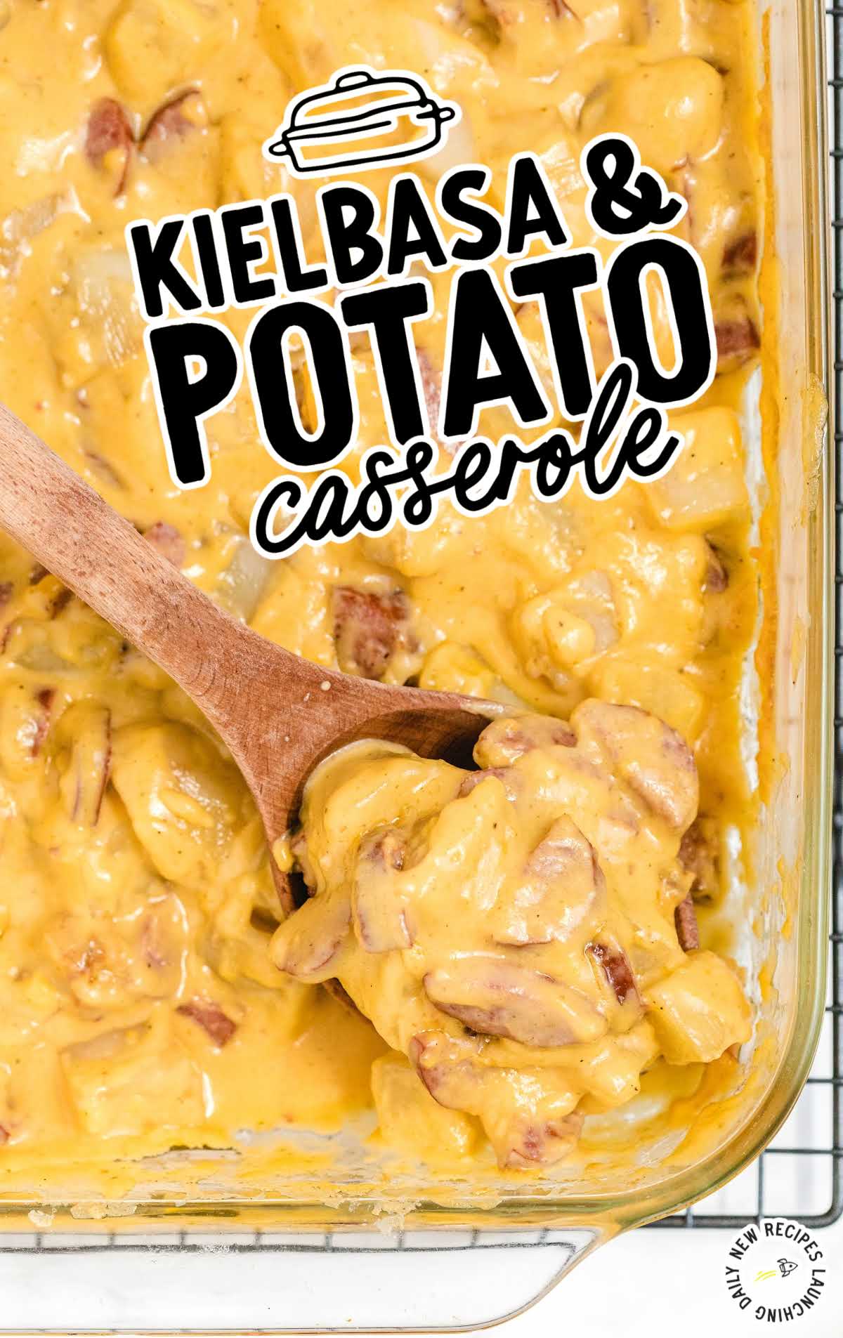 Overhead shot of cheesy kielbasa and potato casserole with a wooden spoon lifting a serving from the dish.