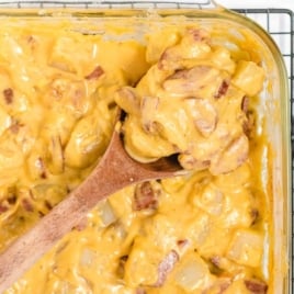Overhead view of kielbasa and potato casserole with a wooden spoon lifting a generous portion from the baking dish.