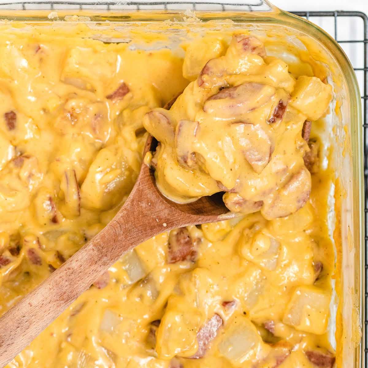 Overhead view of kielbasa and potato casserole with a wooden spoon lifting a generous portion from the baking dish.
