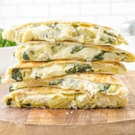 close up shot of spinach artichoke quesadillas stacked on a wooden board
