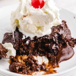close up shot of a piece of Hot Fudge Sundae Cake topped with vanilla ice cream, whip cream, and a cherry on a plate