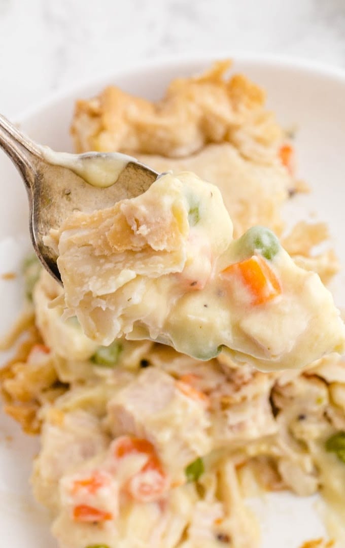 close up shot of chicken pot pie bake on a white plate being picked up with a fork