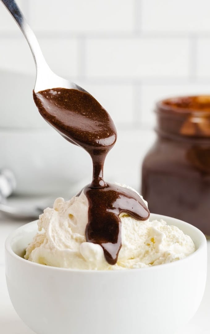 close up side shot of hot fudge sauce being poured with a spoon on to vanilla ice cream in a bowl