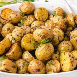 close up shot of roasted potatoes garnished with parsley in a white serving dish