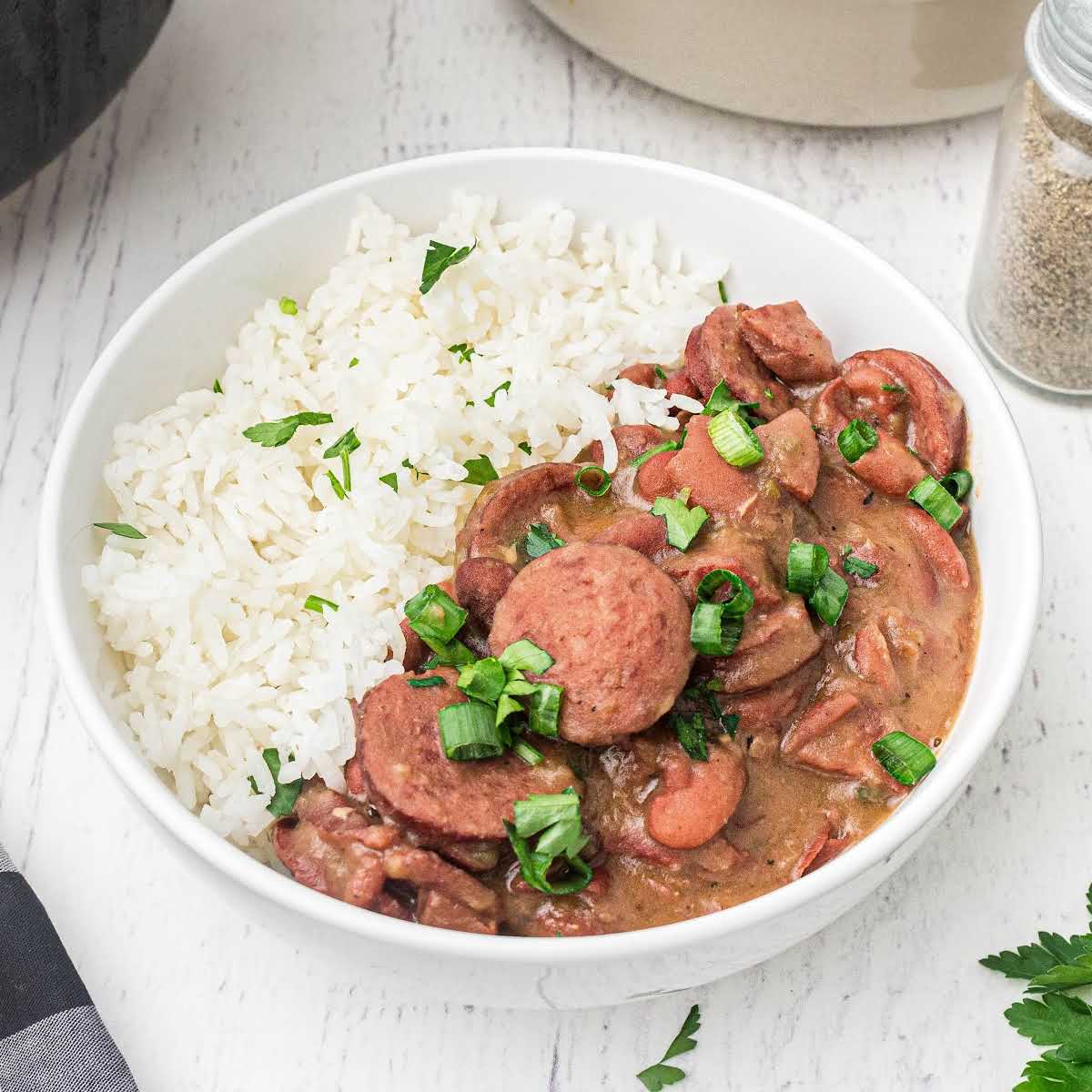 close up shot of a bowl of red beans and rice garnished with green onions and served with white rice
