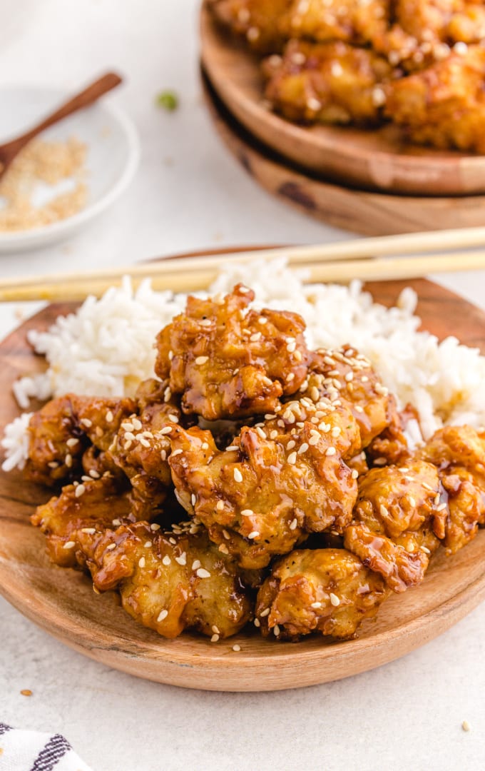 sesame chicken garnished with sesame seeds and served with white rice on a wooden board
