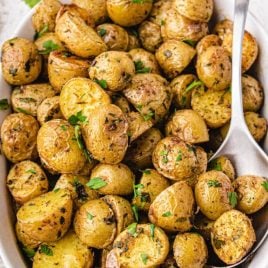 close up overhead shot of garnished oven roasted potatoes in a white dish