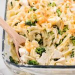 close up shot of chicken broccoli casserole in a baking dish with a wooden spoon