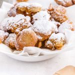 close up shot of funnel cake bites sprinkled with powdered sugar in a white bowl