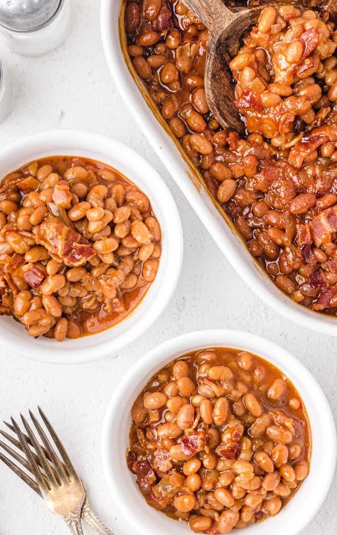 overhead shot of baked beans in white bowls and in a white baking dish with a wooden spoon