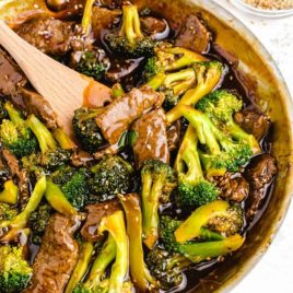 beef and broccoli in a pan with a wooden spoon