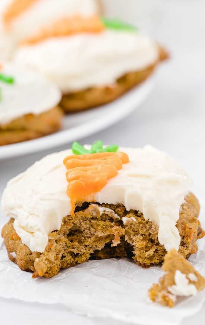 close up shot of carrot cake cookies topped with cream cheese frosting of a carrot with a bite taken out of it
