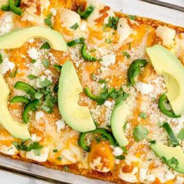close up overhead shot of a baking dish of Chicken Enchiladas garnished with sliced avocados and peppers