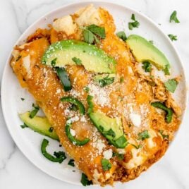 close up overhead shot of a plate of Chicken Enchiladas garnished with sliced avocados and peppers