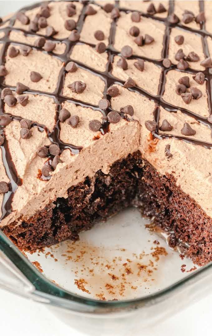 close up shot of chocolate poke cake with a slice taken out of it in a baking dish