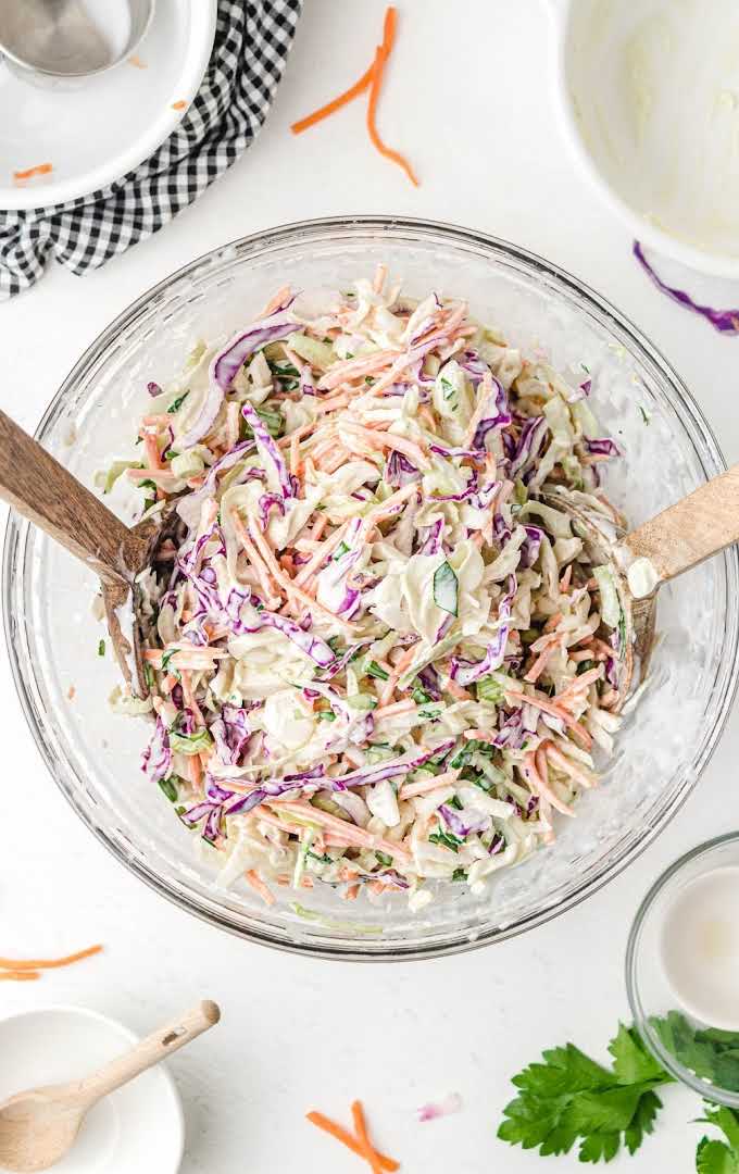 overhead shot classic coleslaw topped with homemade salad dressing in a large bowl with wooden spoons
