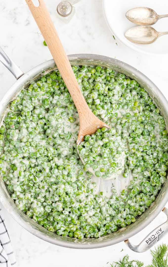overhead shot of creamed peas in a pan with a large wooden spoon