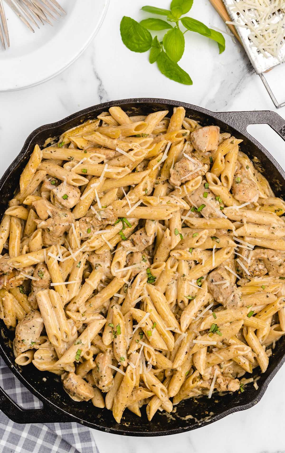 a skillet of chicken pasta garnished with basil
