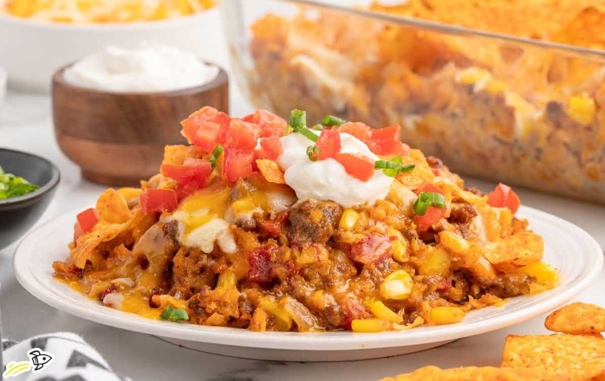 Large scoop of cheesy Dorito casserole being lifted from a glass baking dish.