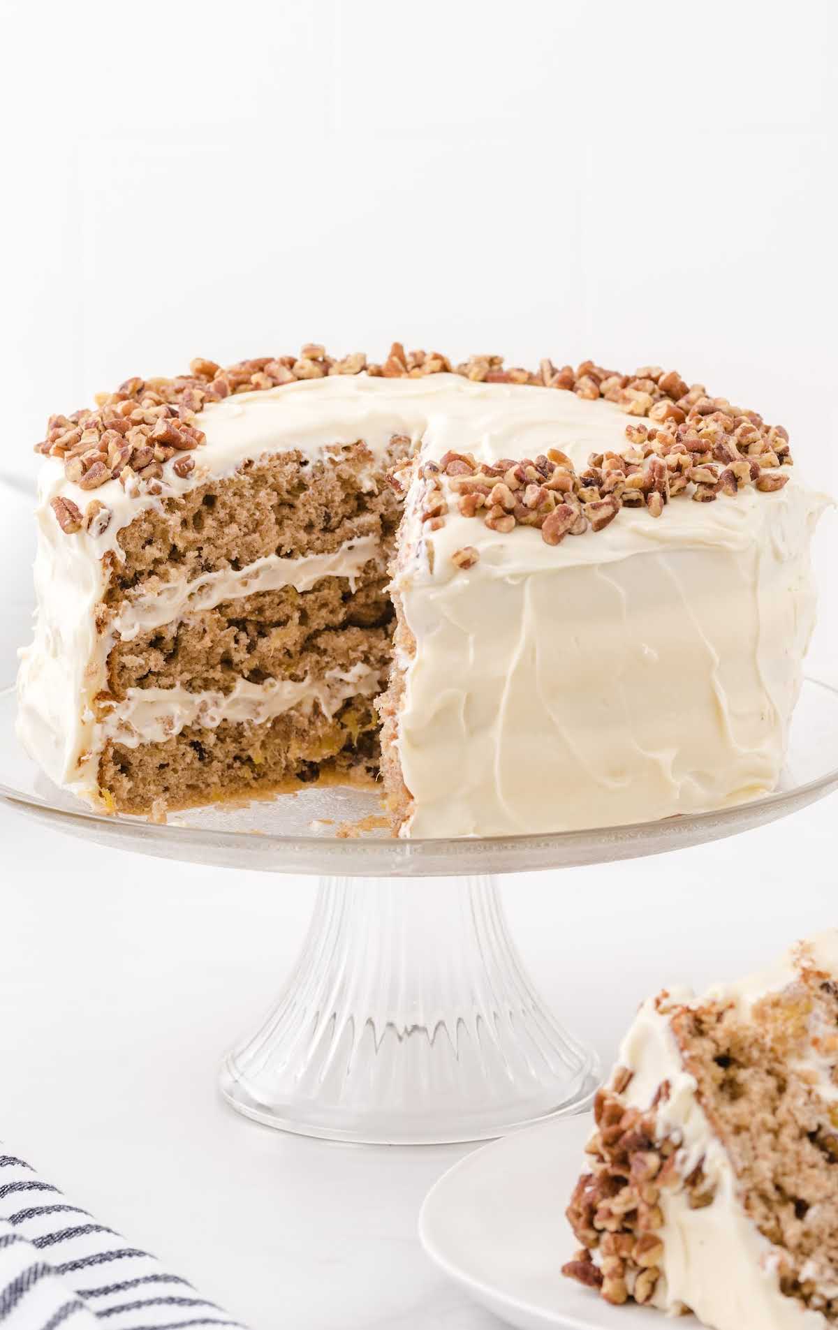 hummingbird cake topped with pecans on a cake stand