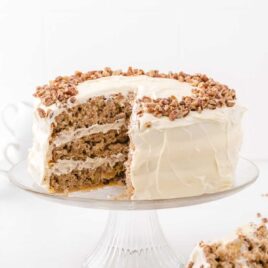 hummingbird cake topped with pecans on a cake stand