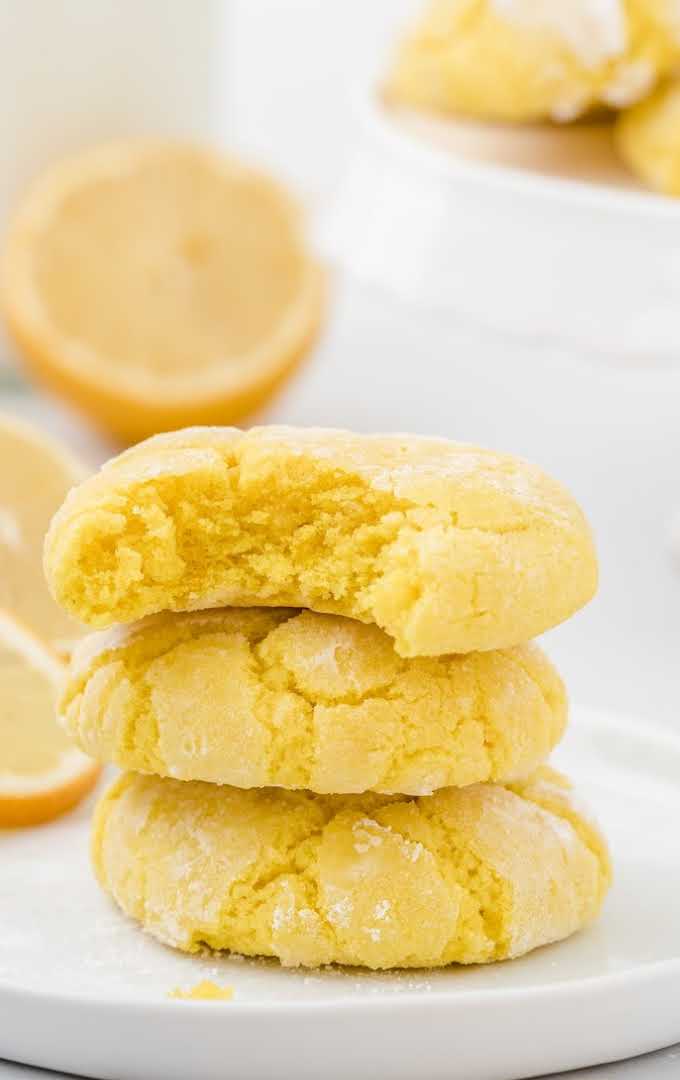 close up shot of lemon crinkle cookies stacked on top of each other on a plate with a bite taken out of one