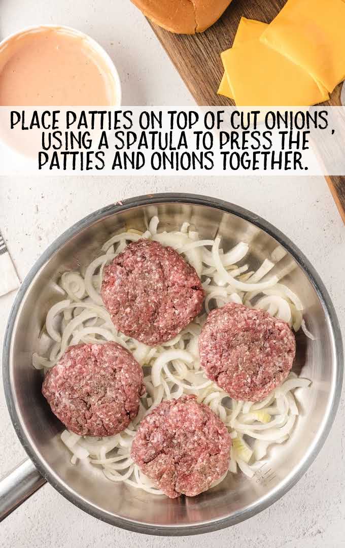 Oklahoma Fried Onion Burgers process shot of raw burgers laid on top of onions on a skillet