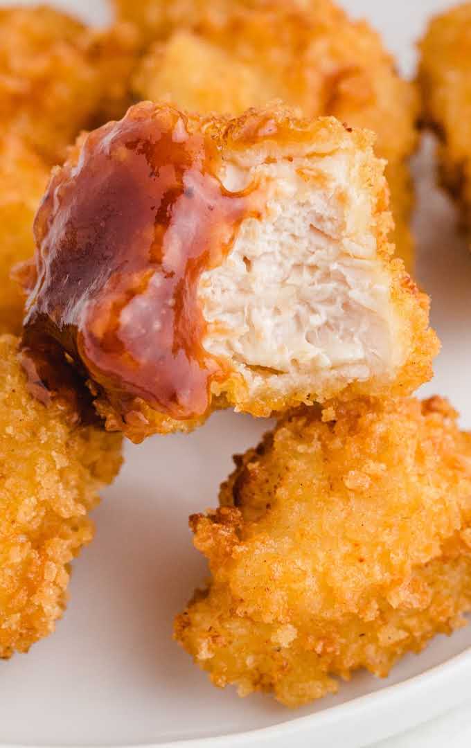 close up shot of popcorn chicken with sauce on a white plate