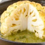 close up shot of the head of a Roasted Cauliflower topped with thyme in a skillet