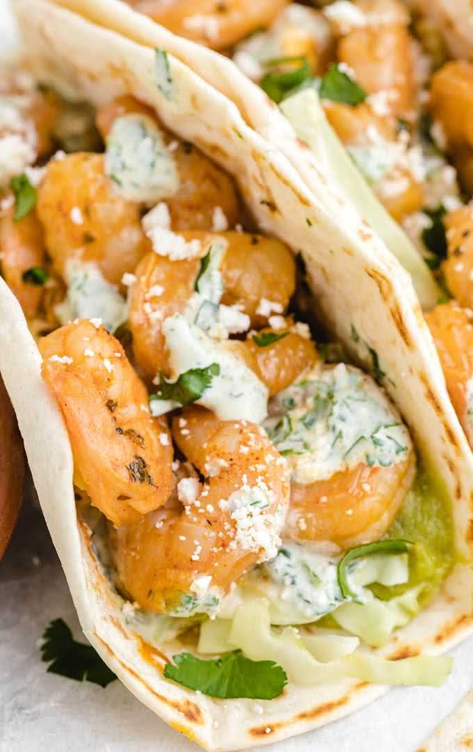 close up side shot of shrimp tacos with spicy cilantro lime sauce topped with cilantro and feta cheese