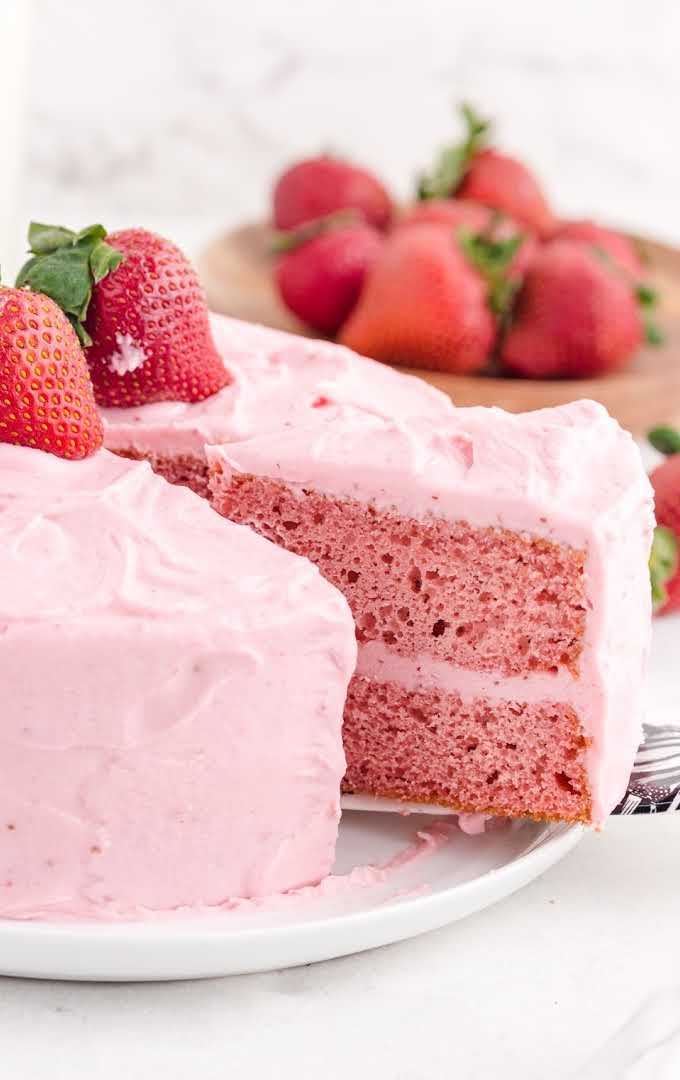 side shot of strawberry cake with a slice being taken out of it with a spatula