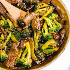 close up overhead shot of beef and broccoli in a pan with a wooden spoon