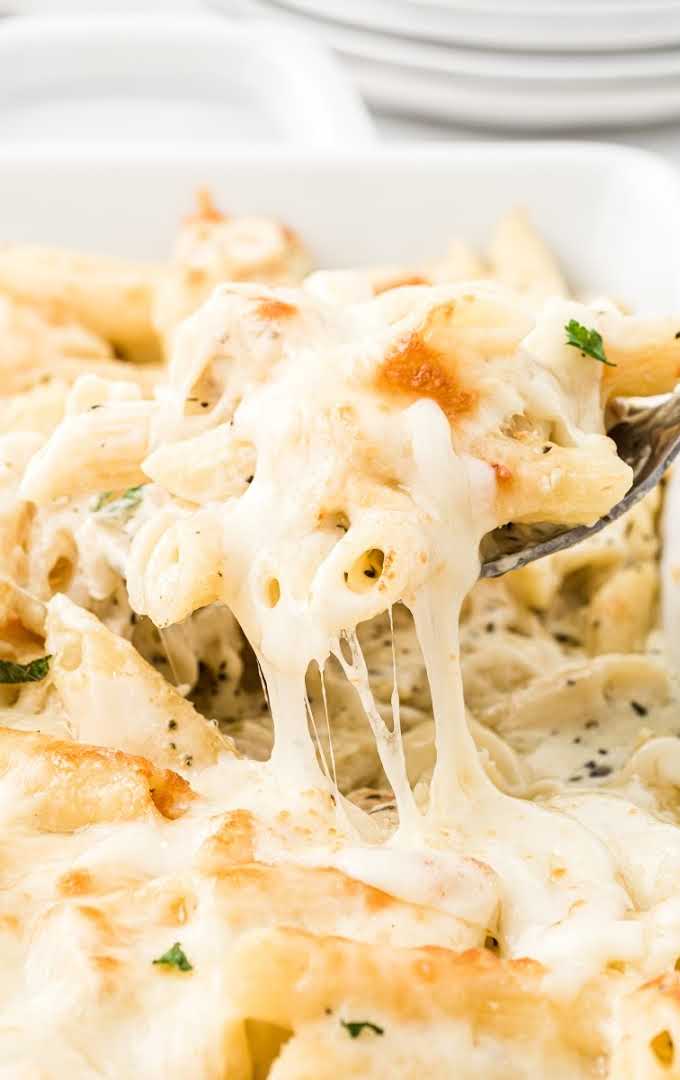 close up shot of creamy chicken alfredo bake being picked with silverware in a baking dish