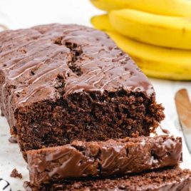 chocolate banana bread with chocolate glaze sliced on a tray with bananas in the background