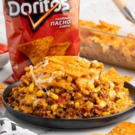 Plate of cheesy Dorito casserole in front of a bag of Doritos with melted cheese, corn, and beef.