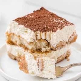 side shot of a slice of easy tiramisu recipe on a plate with a piece taken out with a fork