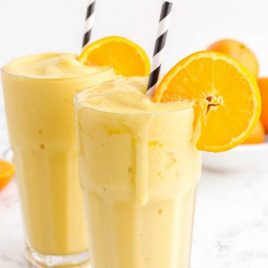 orange julius in glasses with a stripped straw garnished with a slice of orange