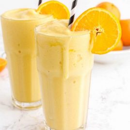 close up side shot of orange julius in glasses with a stripped straw garnished with a slice of orange
