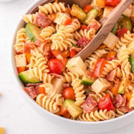 close up shot of pasta salad in a bowl with a wooden spoon