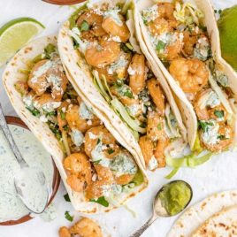overhead shot of shrimp tacos with spicy cilantro lime sauce topped with cilantro and feta cheese with limes on the side