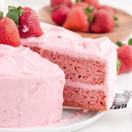 side shot of strawberry cake with a slice being taken out of it with a spatula